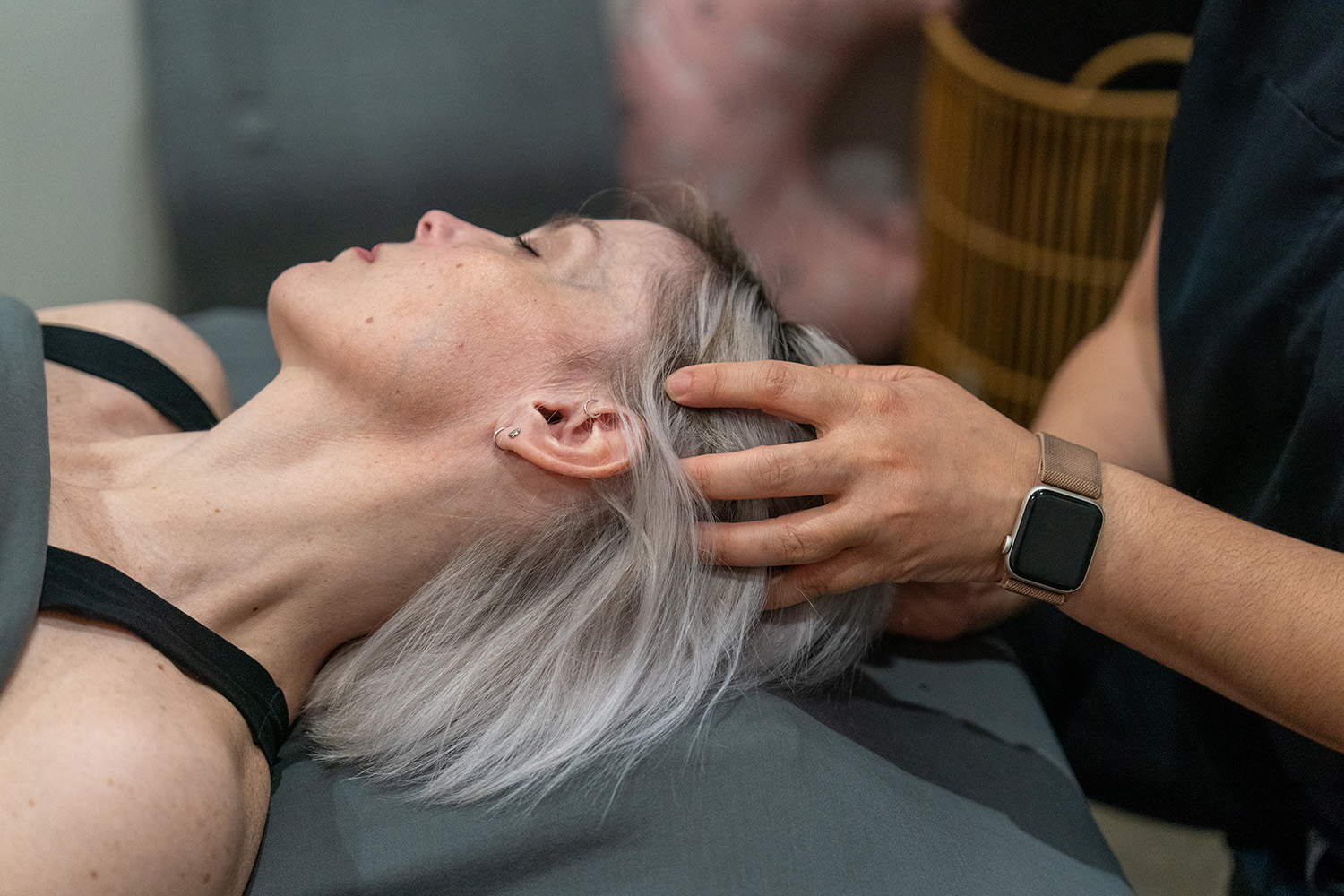 A person receives a head massage while lying down, with a practitioner's hands gently positioned on their scalp.