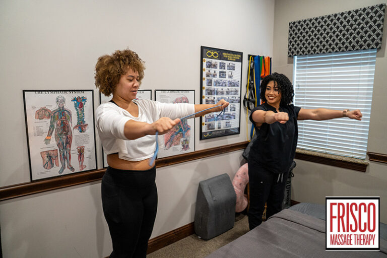 Two women stand side by side in a therapy room, each stretching their arms with resistance bands. Anatomy charts line the wall, while a "Frisco Massage Therapy" logo highlights their focus on therapeutic massage for athletes.