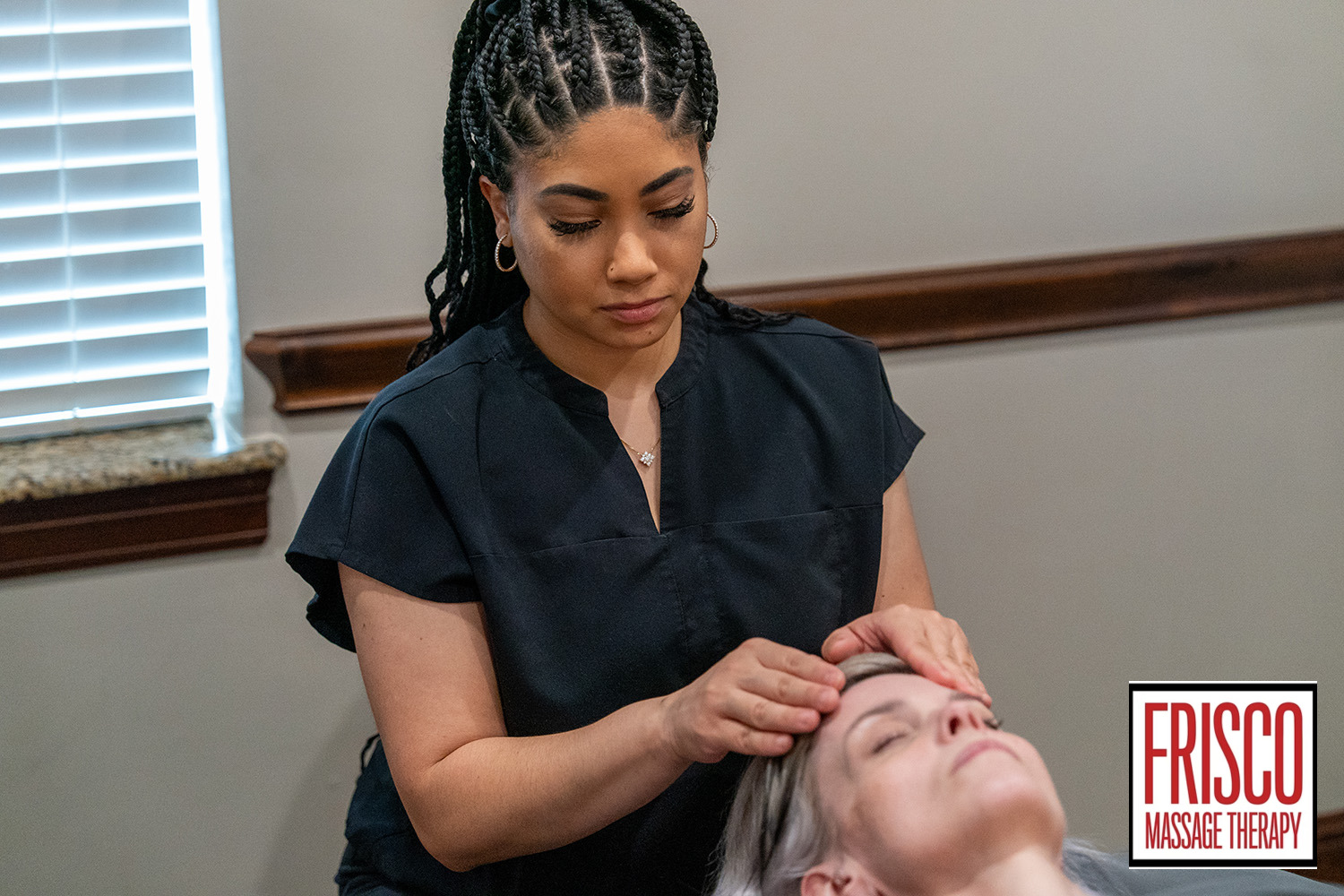 A massage therapist in black attire performs a head massage on a client lying down, showcasing how manual lymphatic drainage aids recovery. The "Frisco Massage Therapy" logo appears in the bottom right corner.