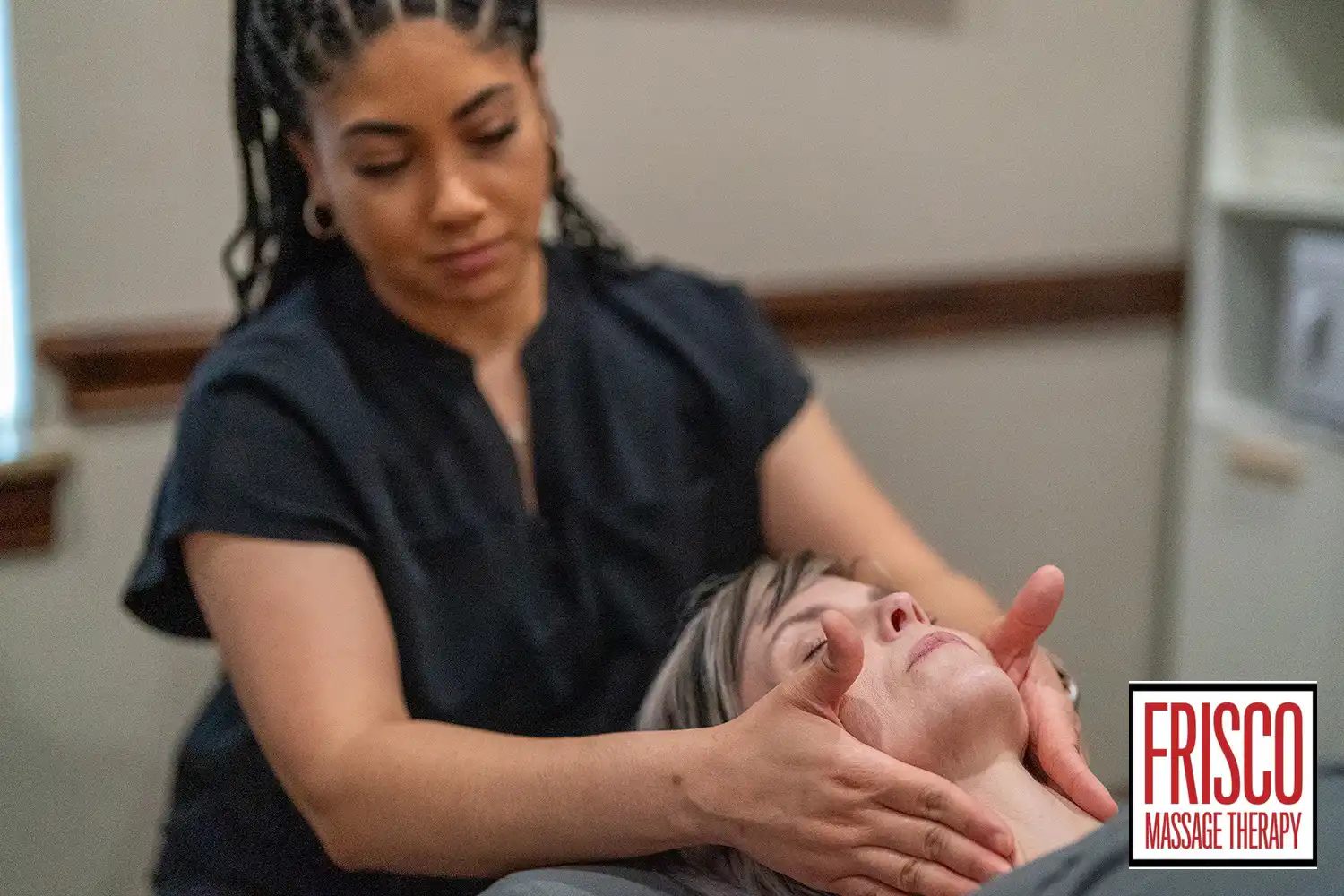 A massage therapist gently provides therapeutic massage for jaw pain, massaging a client's face in a treatment room. The Frisco Massage Therapy logo is visible in the bottom right corner.
