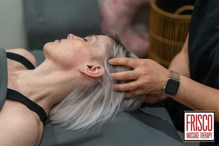 A person with light hair receives a relaxing head massage from a therapist wearing a smartwatch, with the "Frisco Massage Therapy" logo visible in the corner—highlighting manual lymphatic drainage benefits.
