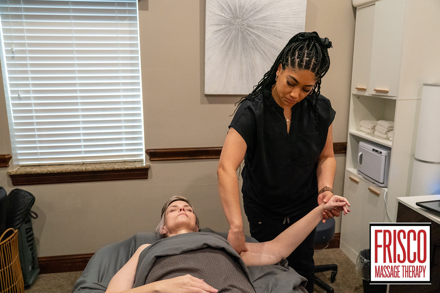 A massage therapist gently stretches a client's arm in a treatment room at Frisco Massage Therapy, offering relief for issues like surgical scar pain.