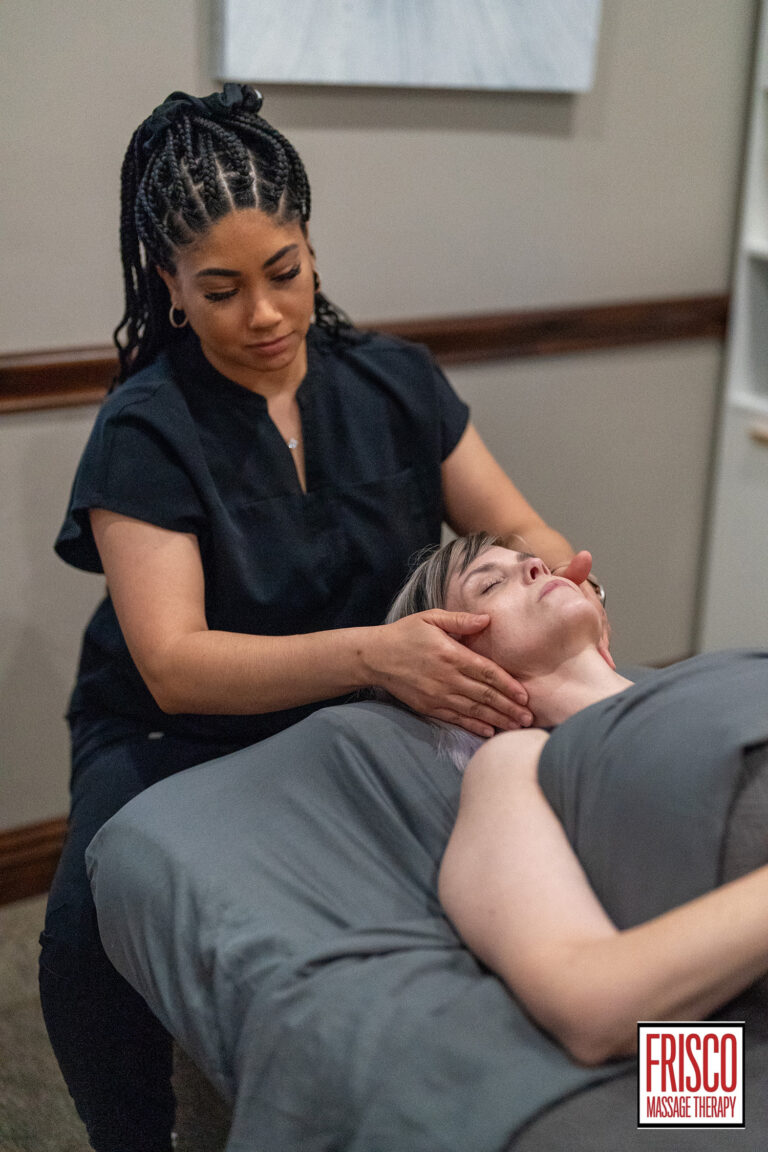 A massage therapist performs a neck massage on a client lying under a gray blanket at a wellness center, highlighting manual lymphatic drainage benefits. The Frisco Massage Therapy logo is visible in the corner.