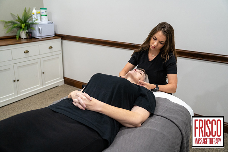A massage therapist works on a client's neck in a treatment room at Frisco Massage Therapy, providing therapeutic massage for jaw pain.
