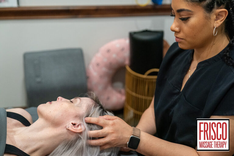 A massage therapist gently massages a client's head to promote mobility while the client lies on a table. The Frisco Massage Therapy logo is visible in the bottom right corner.