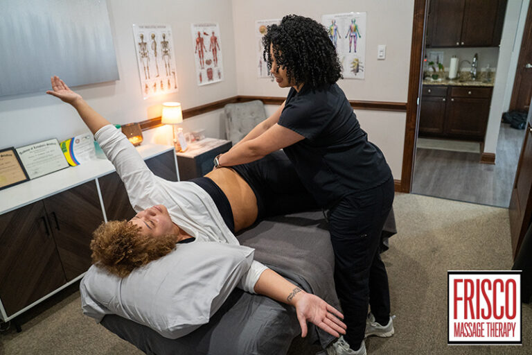 A massage therapist assists a client with a stretching exercise on a massage table in a therapy room, demonstrating the benefits of Frisco sports massage therapy. The “Frisco Massage Therapy” logo is visible in the bottom right corner.