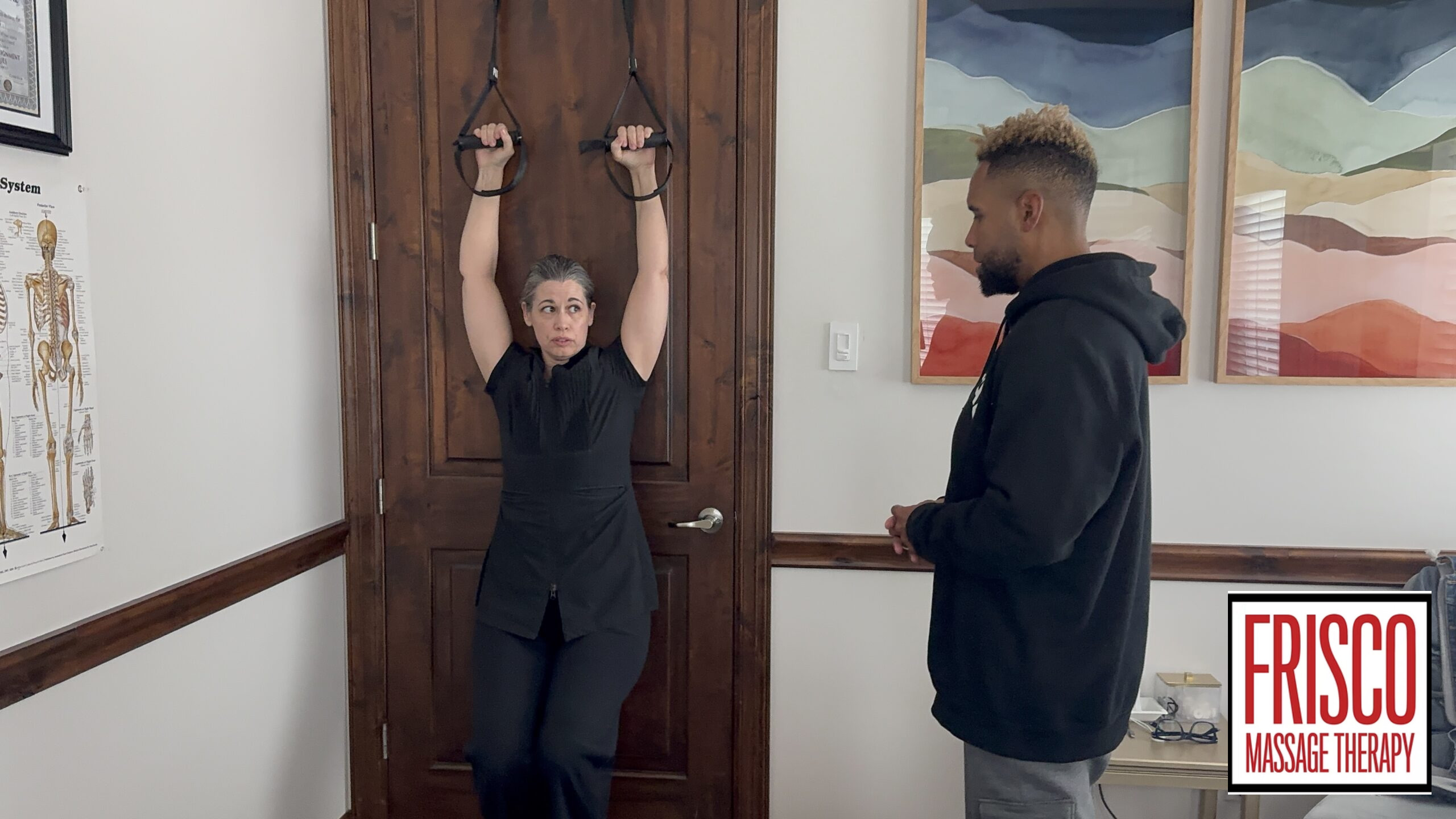 A woman hangs from fitness rings attached to a door while a man stands nearby observing, emphasizing the importance of athlete care. A Frisco Massage Therapy sign is visible in the lower right corner.