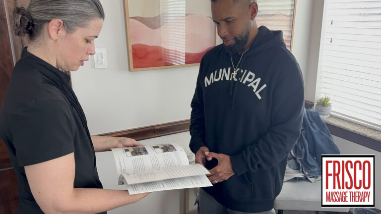 A woman shows a man an open booklet in an office. The man wears a black hoodie, perhaps discussing the benefits of Frisco sports massage therapy. The Frisco Massage Therapy logo is visible in the bottom right corner.