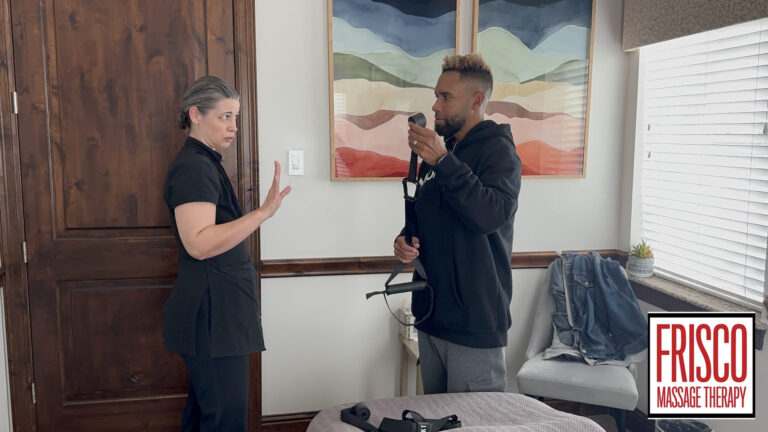 A woman holds up her hand to stop a man holding a massage tool in a therapy room with the Frisco Massage Therapy logo visible, highlighting the importance of communication during therapeutic massage for optimal recovery and athletic performance.