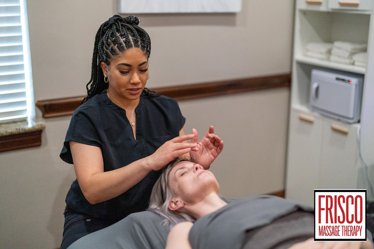 A massage therapist performs a manual lymphatic drainage facial massage on a client lying on a table in a spa room. The Frisco Massage Therapy logo is visible in the corner, highlighting the benefits of this relaxing treatment.