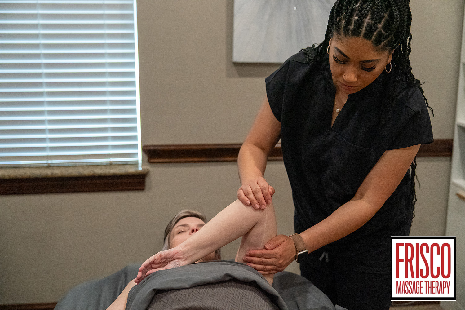 A massage therapist stretches a client’s arm during a session in a treatment room, demonstrating how therapeutic massage helps scar tissue heal and improve flexibility. The Frisco Massage Therapy logo is visible in the lower right corner.