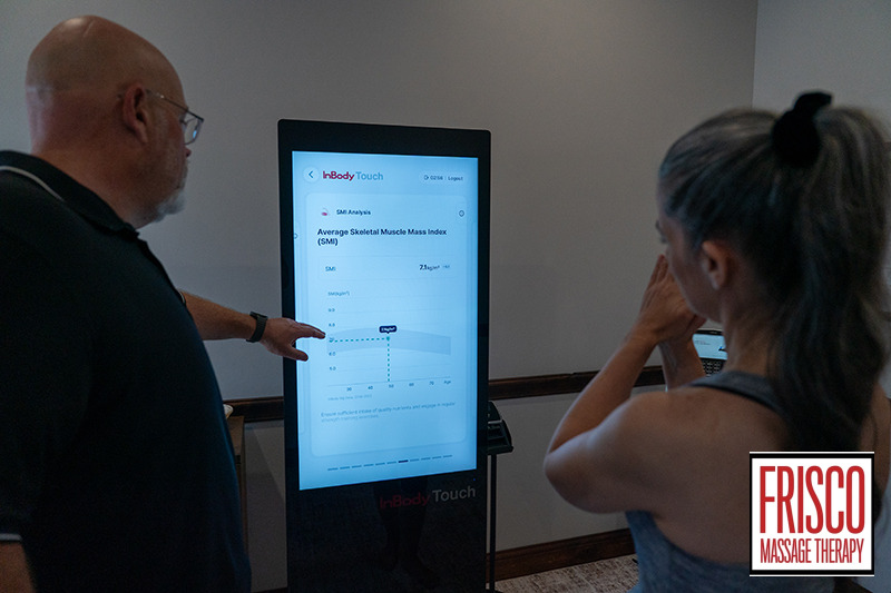 Two people look at a digital health analysis screen displaying a muscle mass index chart and body composition analysis at Frisco Massage Therapy.