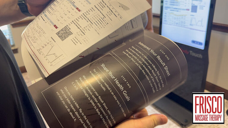 Person holding an open brochure with health charts and body composition analysis in front of a computer screen; Frisco Massage Therapy logo visible in the bottom right corner.
