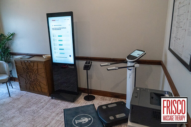 An InBody 580 body composition analysis machine and a digital health monitor are set up in a small office room with a plant, cabinet, and Frisco Massage Therapy sign visible.
