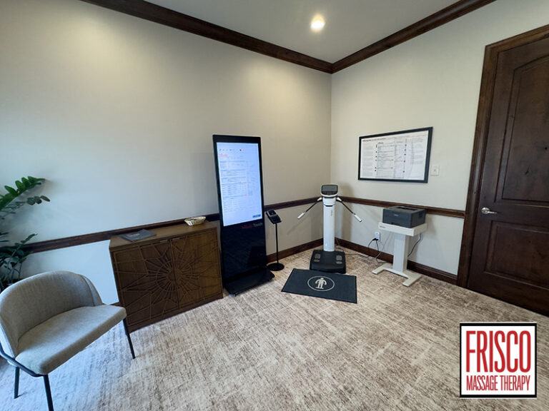 Small office with a chair, cabinet, standing digital screen, scale for InBody 580 body composition analysis Frisco, printer, framed chart, plant, and “Frisco Massage Therapy” logo in the corner.