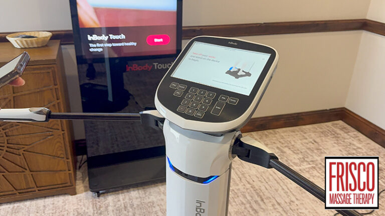 A digital body composition analyzer with a touchscreen and handles is shown in an office setting, featuring a Frisco Massage Therapy logo in the corner. This advanced device makes it easy to track body composition while on GLP-1 medication, supporting clients on their wellness journey.