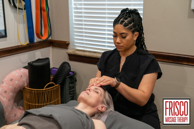 A massage therapist performs a facial massage on a client lying down in a treatment room, demonstrating an understanding of lymphatic drainage massage techniques. The Frisco Massage Therapy logo appears in the bottom right corner.