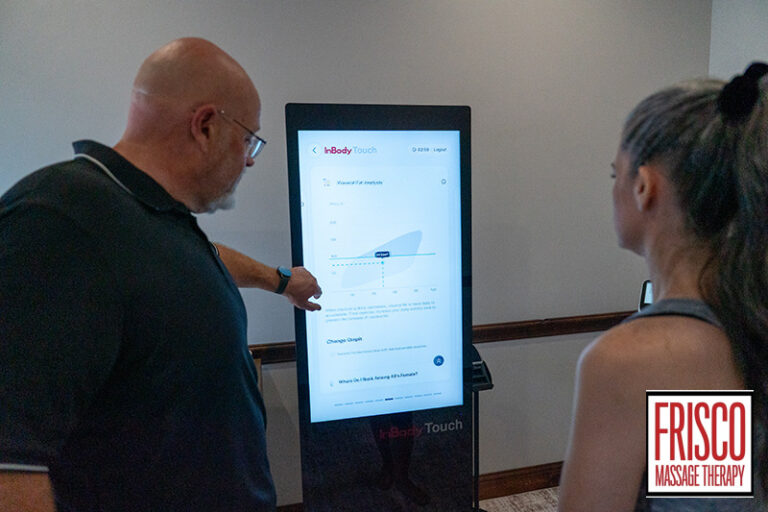 A man points to a data graph on a touchscreen display while a woman watches; a Frisco Massage Therapy logo is visible in the corner, highlighting their focus on body composition analysis.