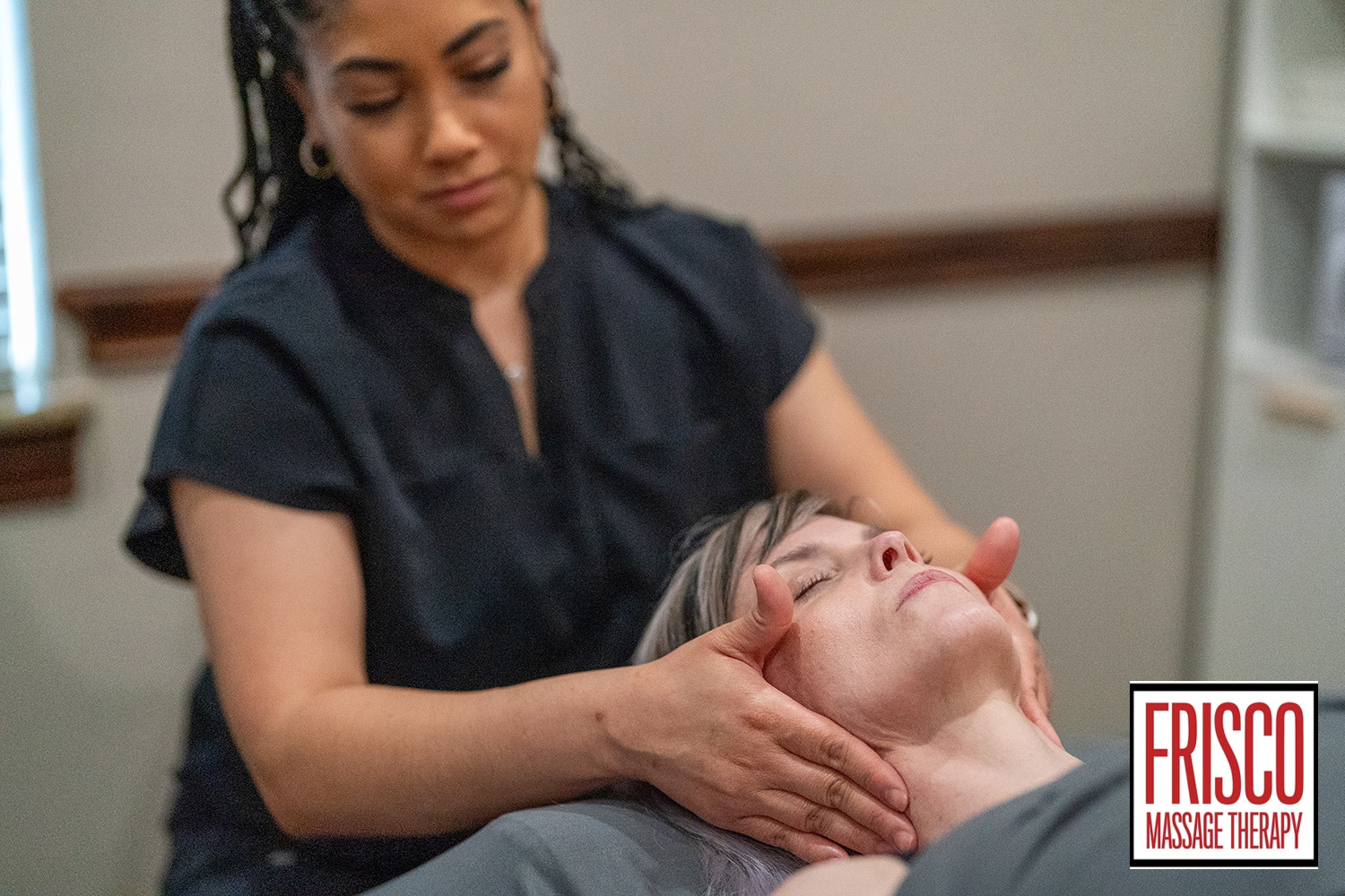 A massage therapist performs a neck and head massage on a client lying down, demonstrating an understanding of lymphatic drainage massage techniques. The Frisco Massage Therapy logo is visible in the bottom right corner.