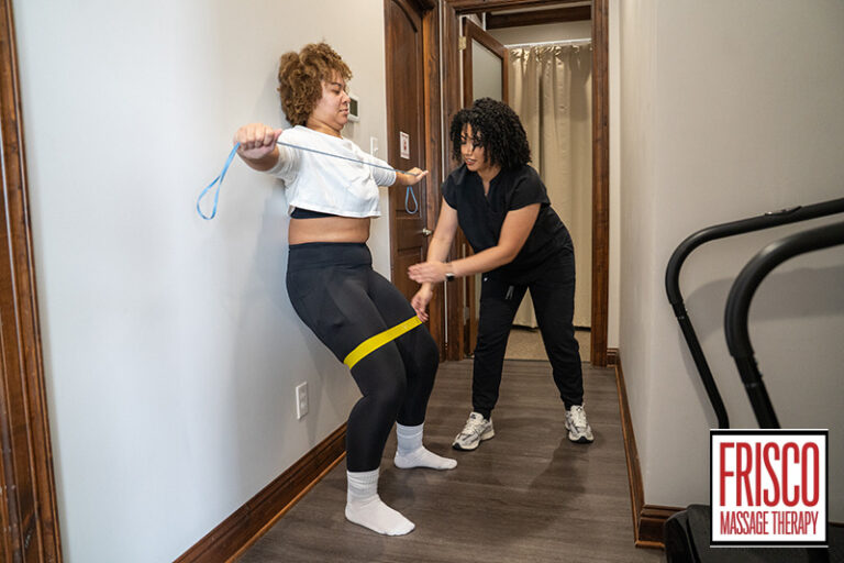 A physical therapist supervises a client performing wall-assisted squats with resistance bands during sports therapy massage in Frisco.