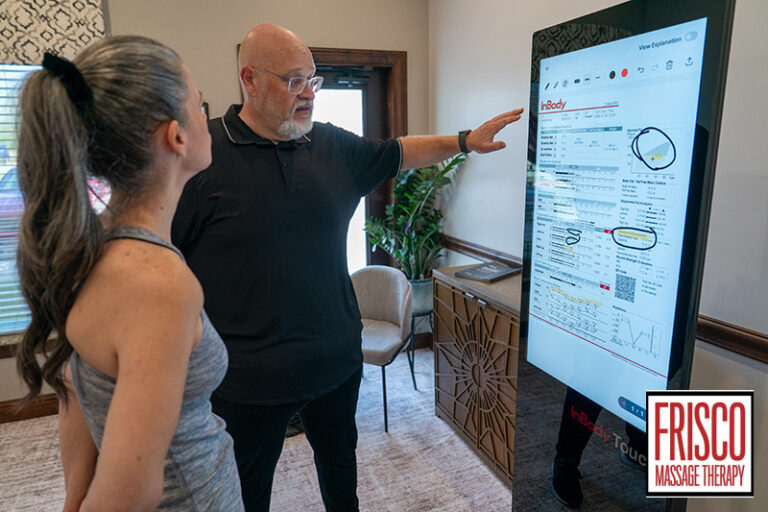 A man points to a digital body composition analysis screen while explaining the data to a woman.