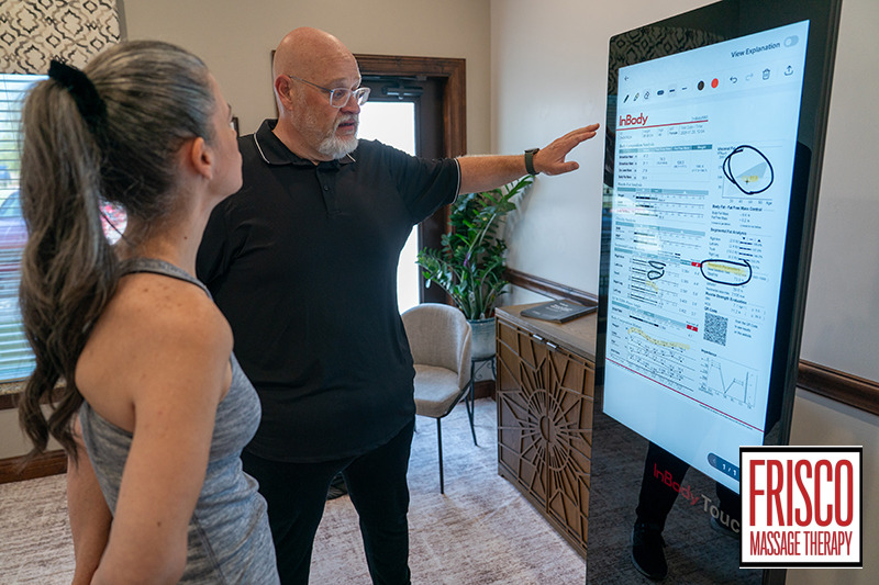 A man points to a digital body composition analysis screen while explaining the data to a woman.